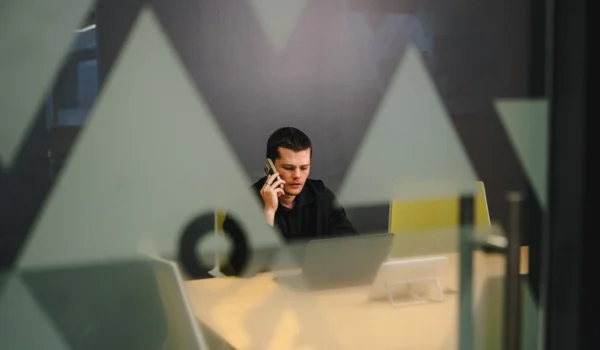 IT director on a phone call at a conference table, reviewing compliance obligations now that CMMC Phase 2 suspended its third-party assessment requirement