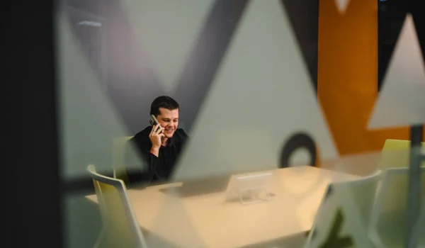 INVITE employee on a phone call in a conference room, video touch panel visible through the office's frosted triangle glass pattern