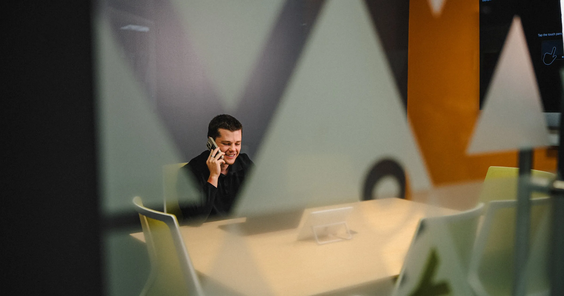 INVITE employee on a phone call in a conference room, video touch panel visible through the office's frosted triangle glass pattern