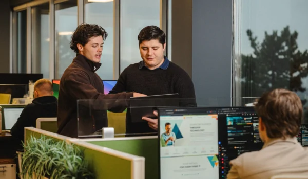 Two INVITE Networks employees reviewing a tablet together in an open office, discussing Microsoft Copilot Autopilot readiness