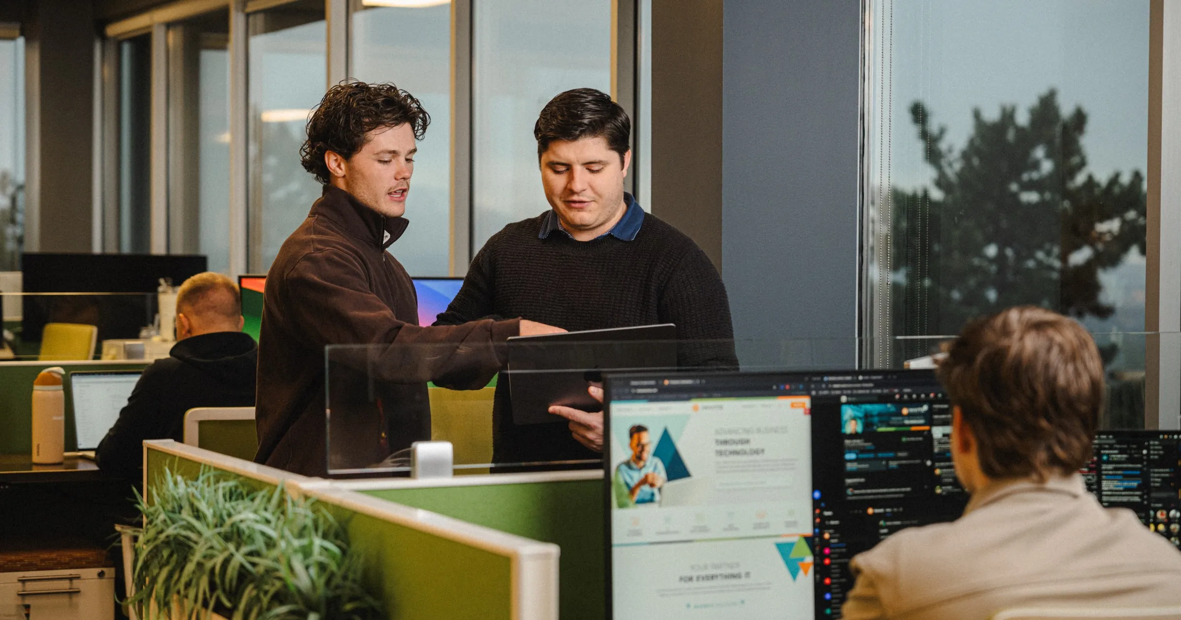 Two INVITE Networks employees reviewing a tablet together in an open office, discussing Microsoft Copilot Autopilot readiness